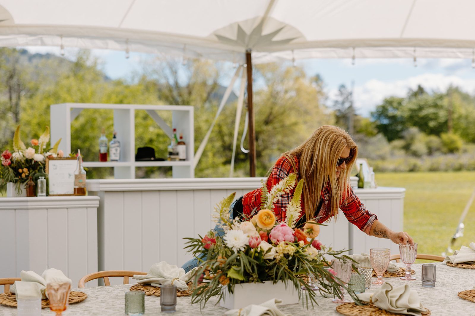 A woman is arranging flowers on a table under a tent.