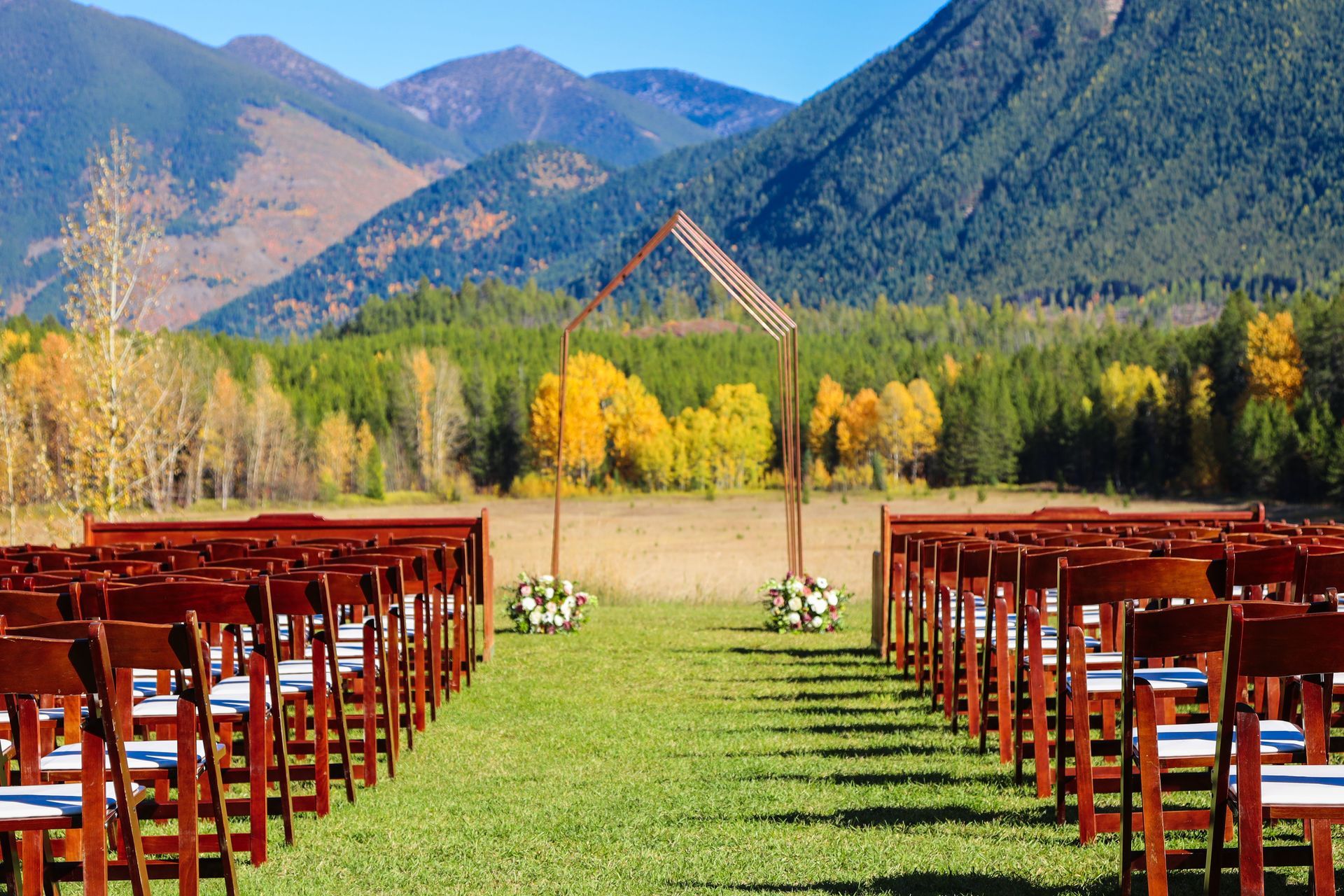 A row of wooden chairs are lined up in a field with mountains in the background.