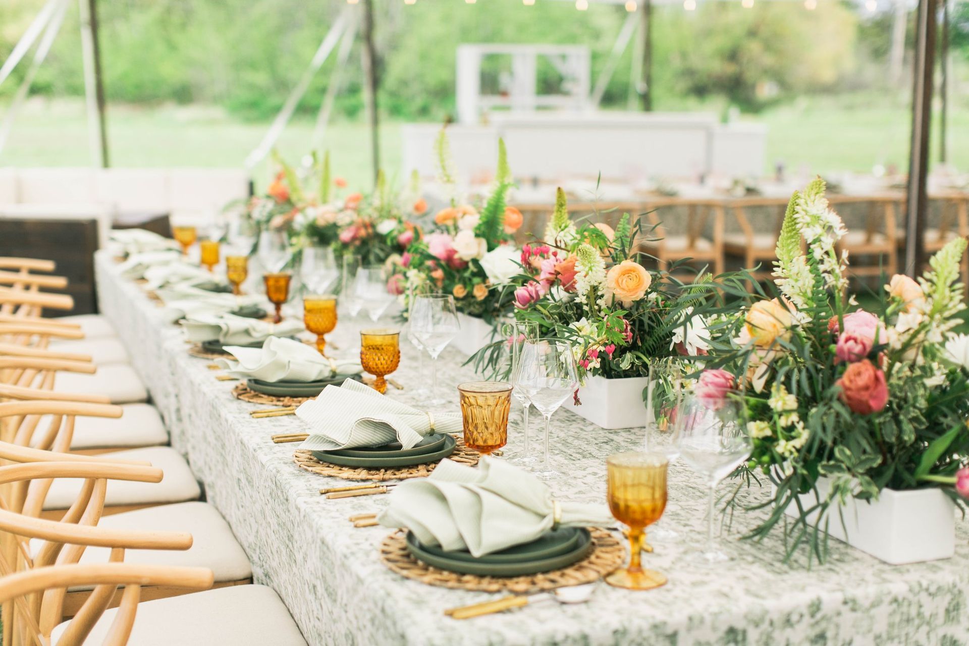 A long table with plates , glasses , napkins and flowers on it.