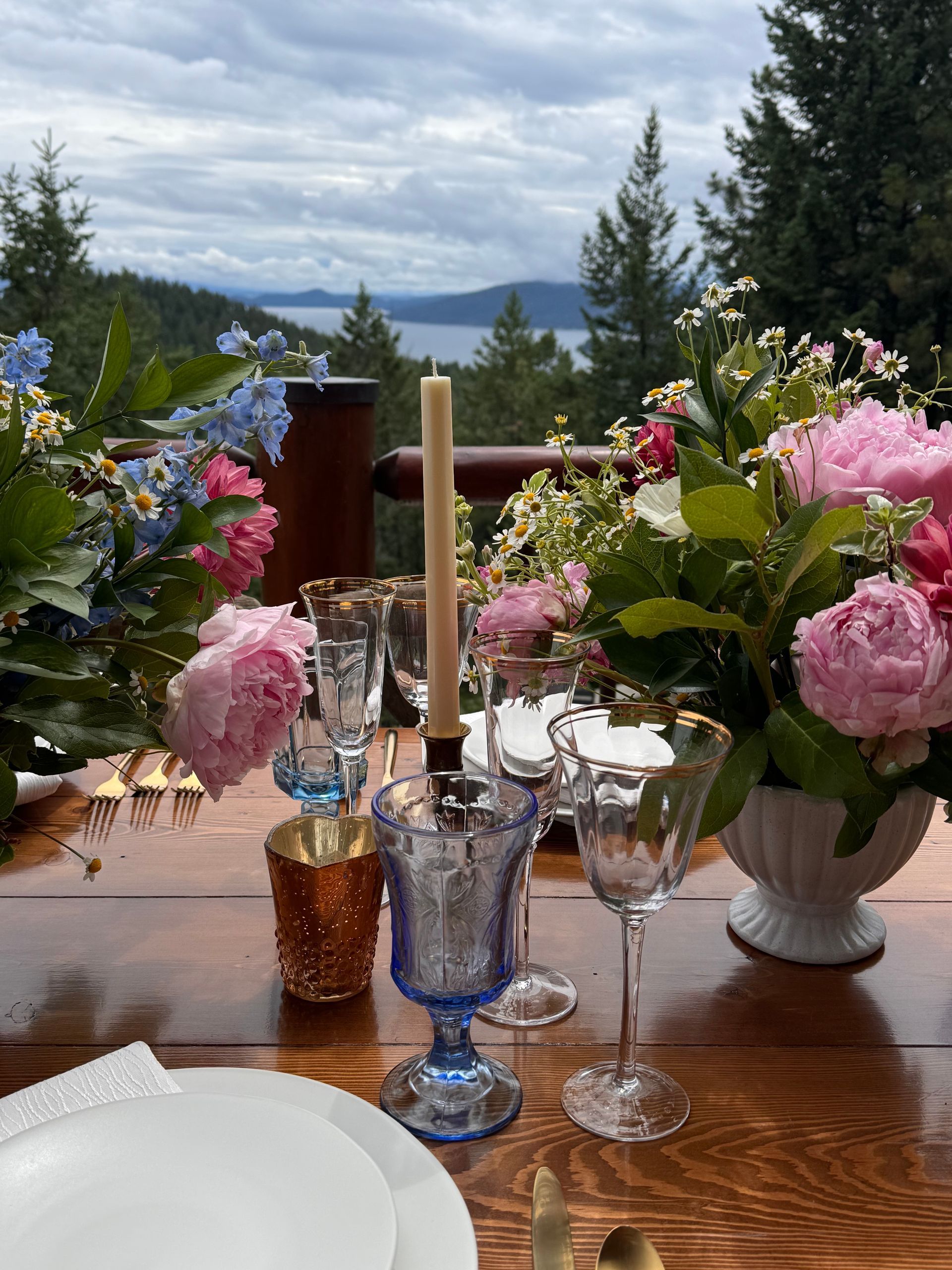 A wooden table with plates , glasses , candles and flowers on it.