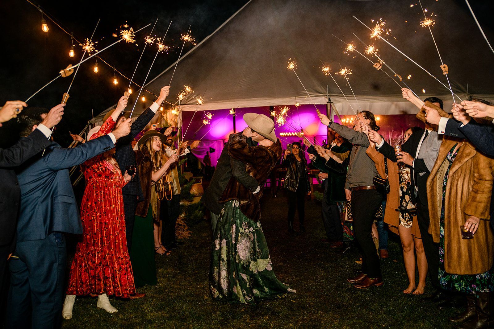 A bride and groom are kissing in front of a crowd of people holding sparklers.