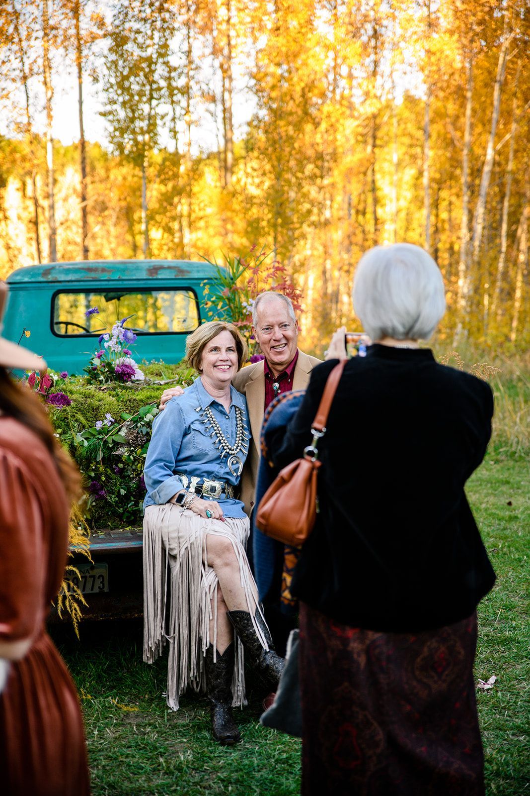 A woman is taking a picture of a man and woman sitting in the back of a truck.