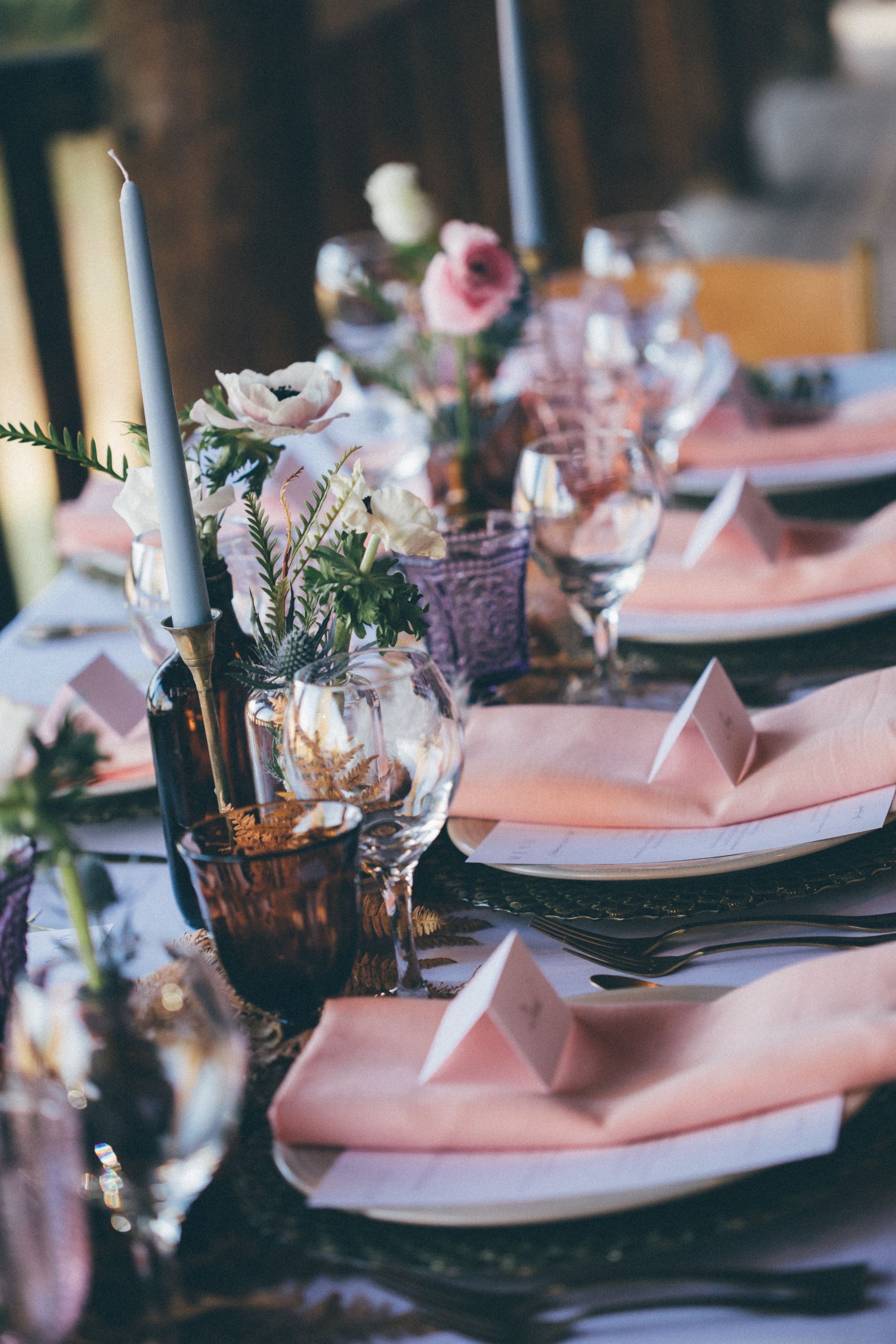 A table set for a wedding reception with plates , napkins , candles and flowers.