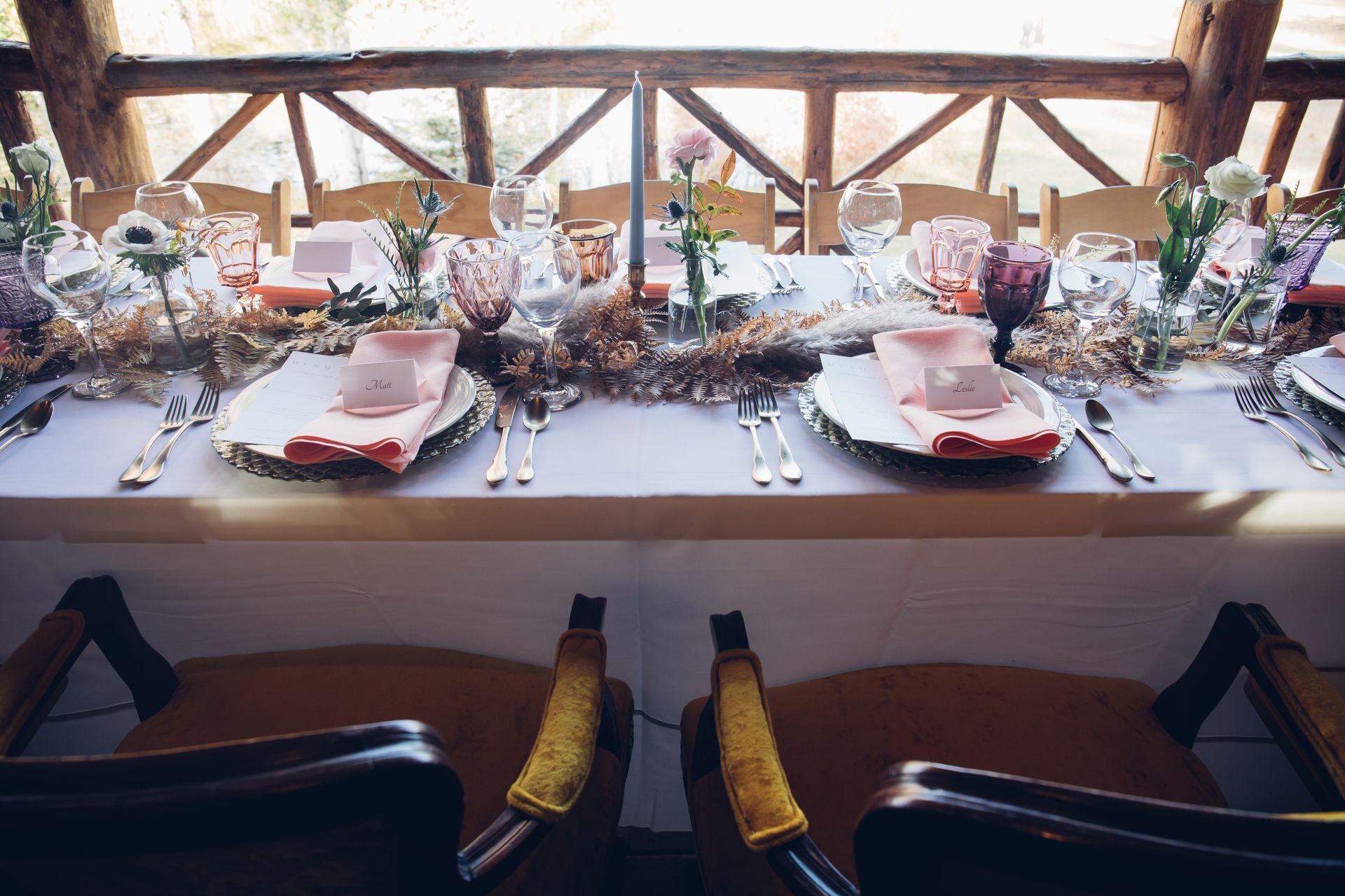 A long table with plates , utensils , and flowers on it.