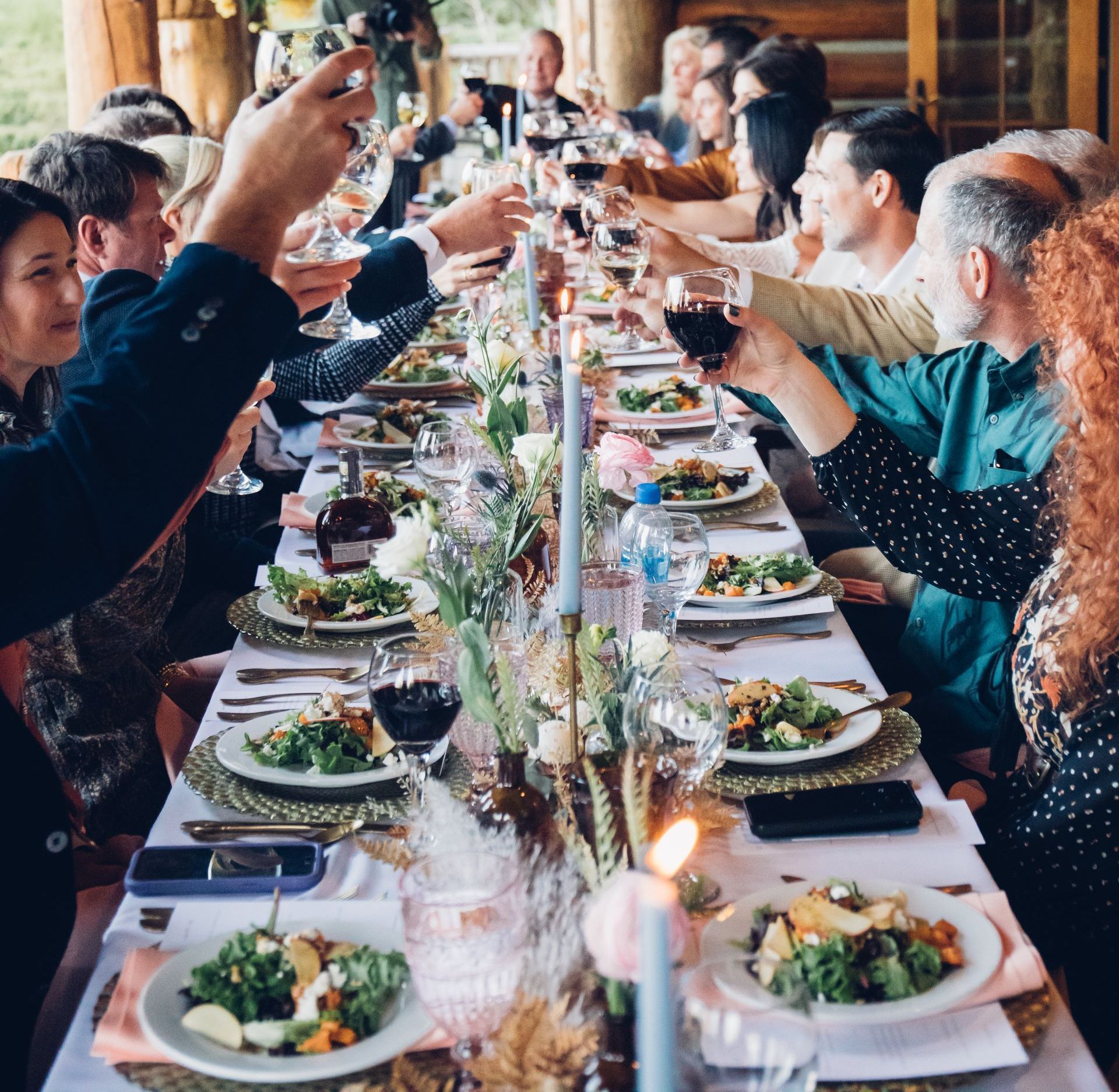 A group of people sitting at a long table toasting with wine glasses