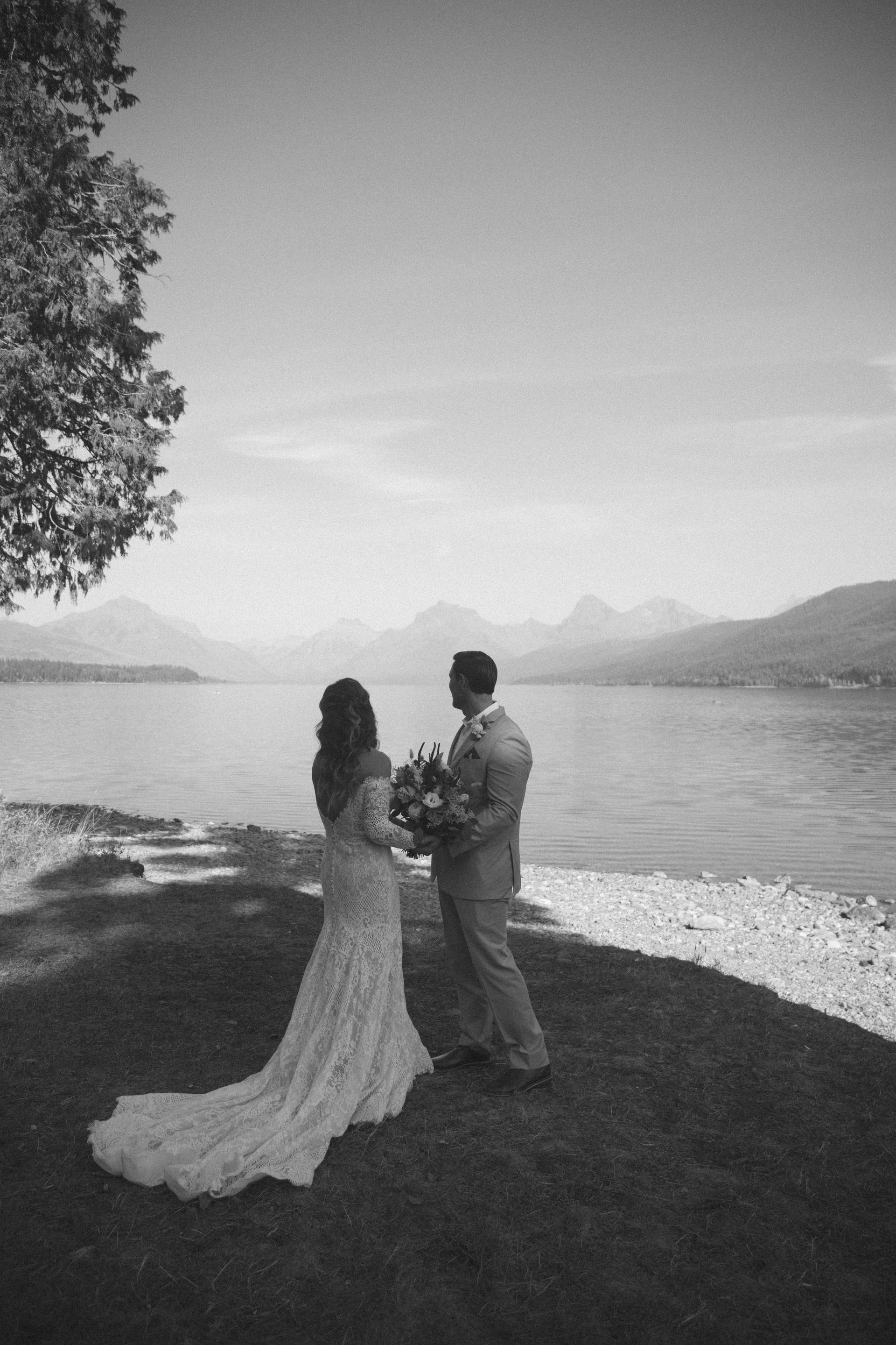 A black and white photo of a bride and groom standing next to a lake.