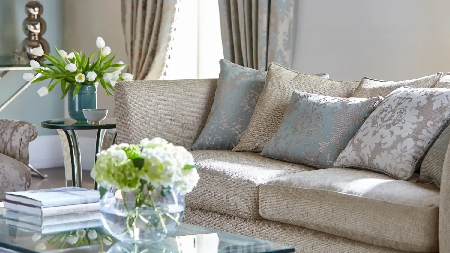 A living room with a couch and a glass coffee table with a vase of flowers on it.