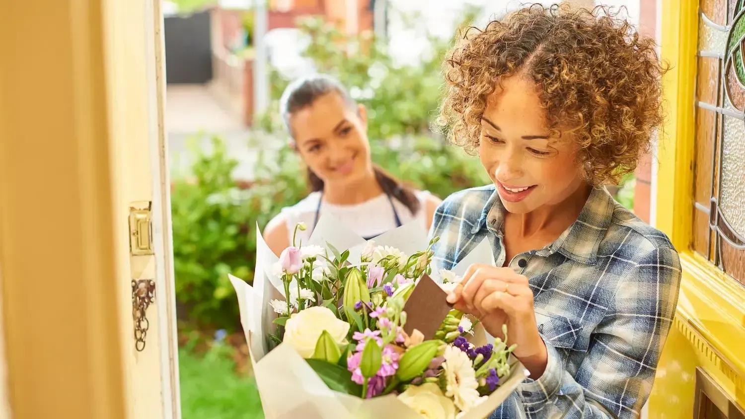 Woman receiving a bouquet of flowers at her front door. A delivery person smiles in the background.