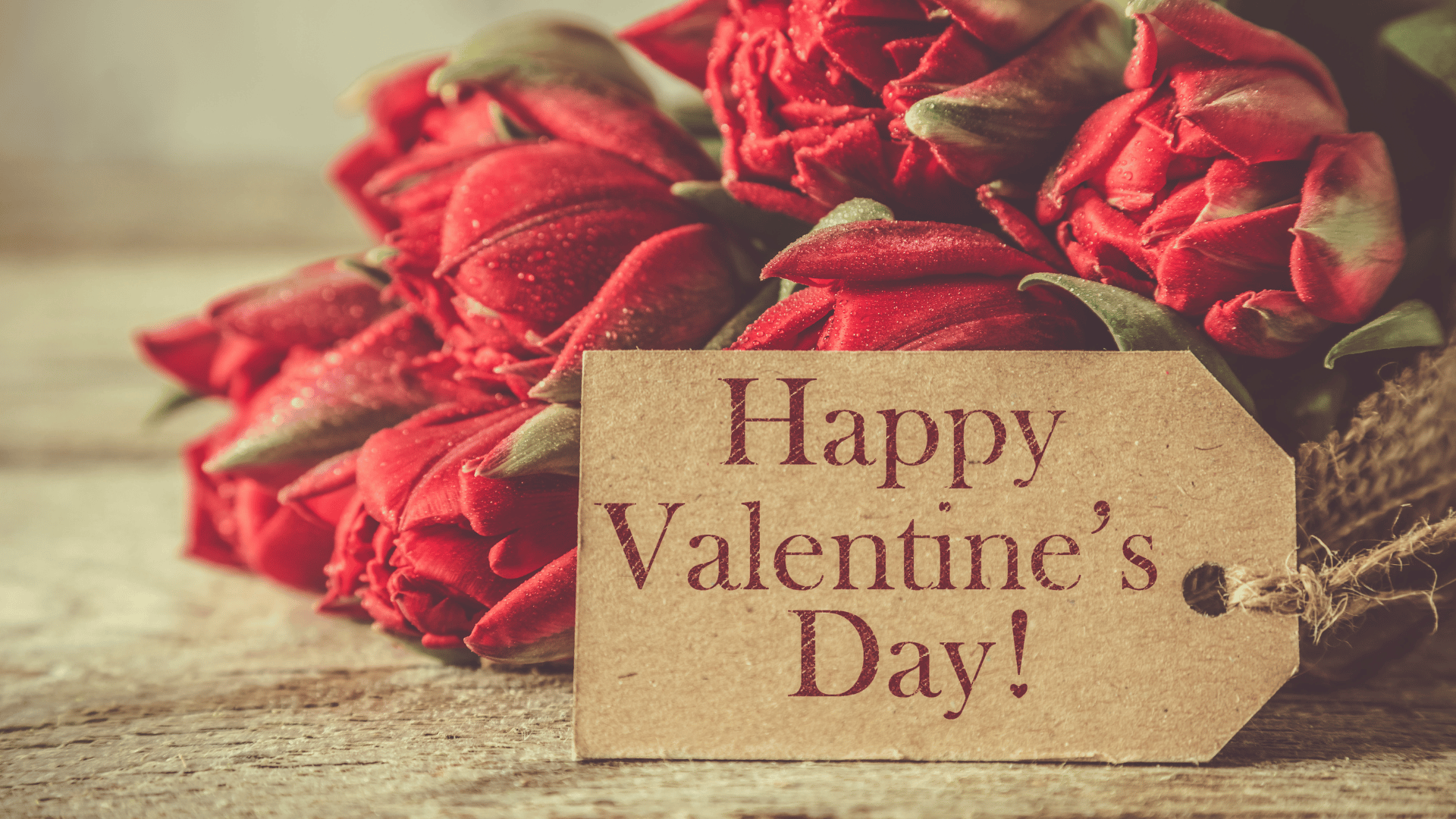 a bouquet of red roses with a happy valentine 's day tag on a wooden table .
