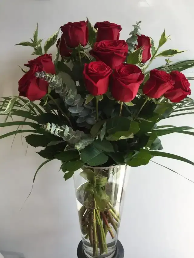 a vase filled with red roses and greenery