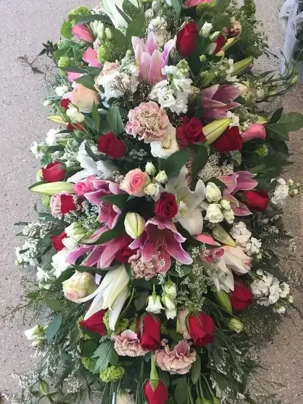 Floral funeral spray with pink lilies, red roses, and white blooms on a gray background