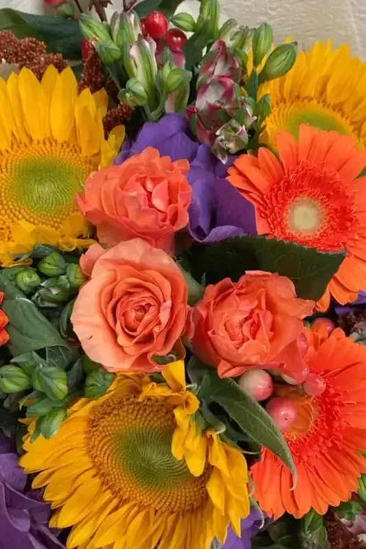 Sunflowers, orange gerbera daisies, and peach roses in a colorful floral arrangement.