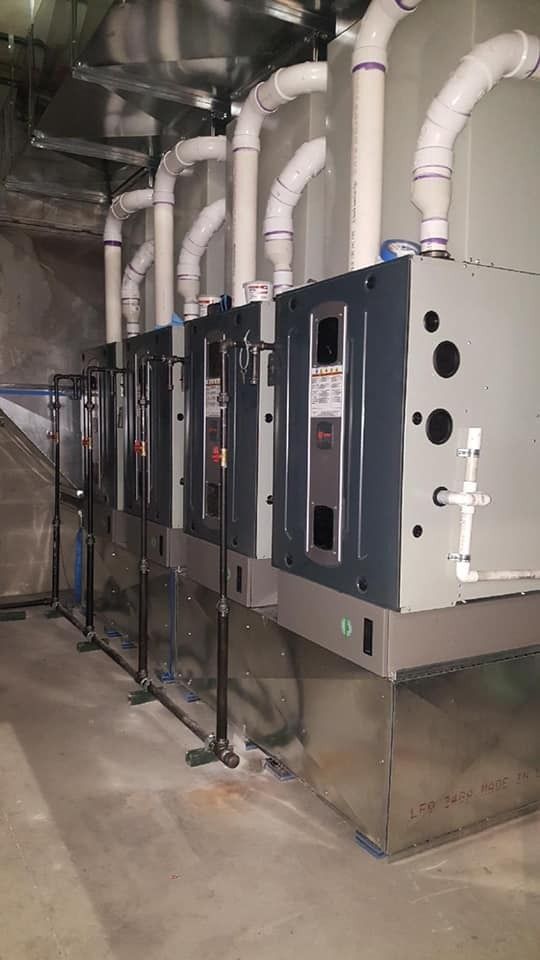 Row of gray HVAC units with white PVC ductwork in a utility room.