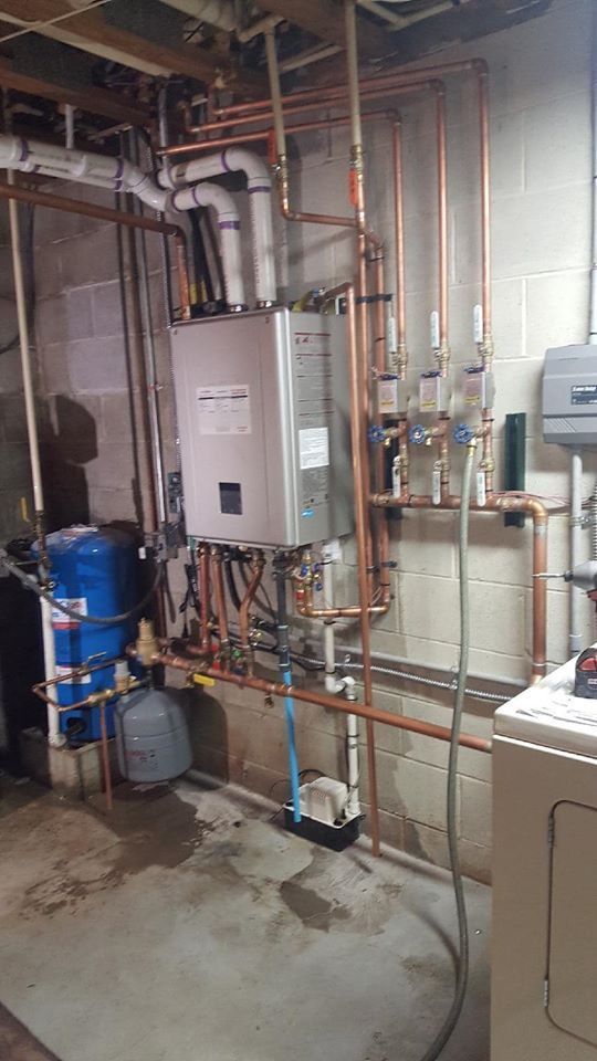 Copper pipes and a tankless water heater installed on a basement wall.