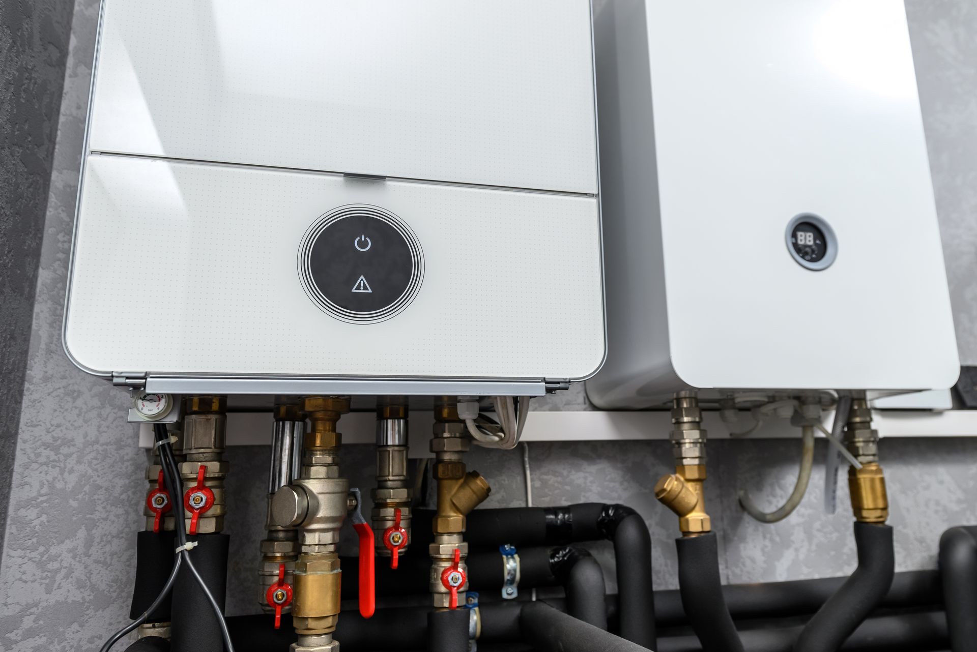 Two white gas boilers with connected pipes and valves in a utility room.