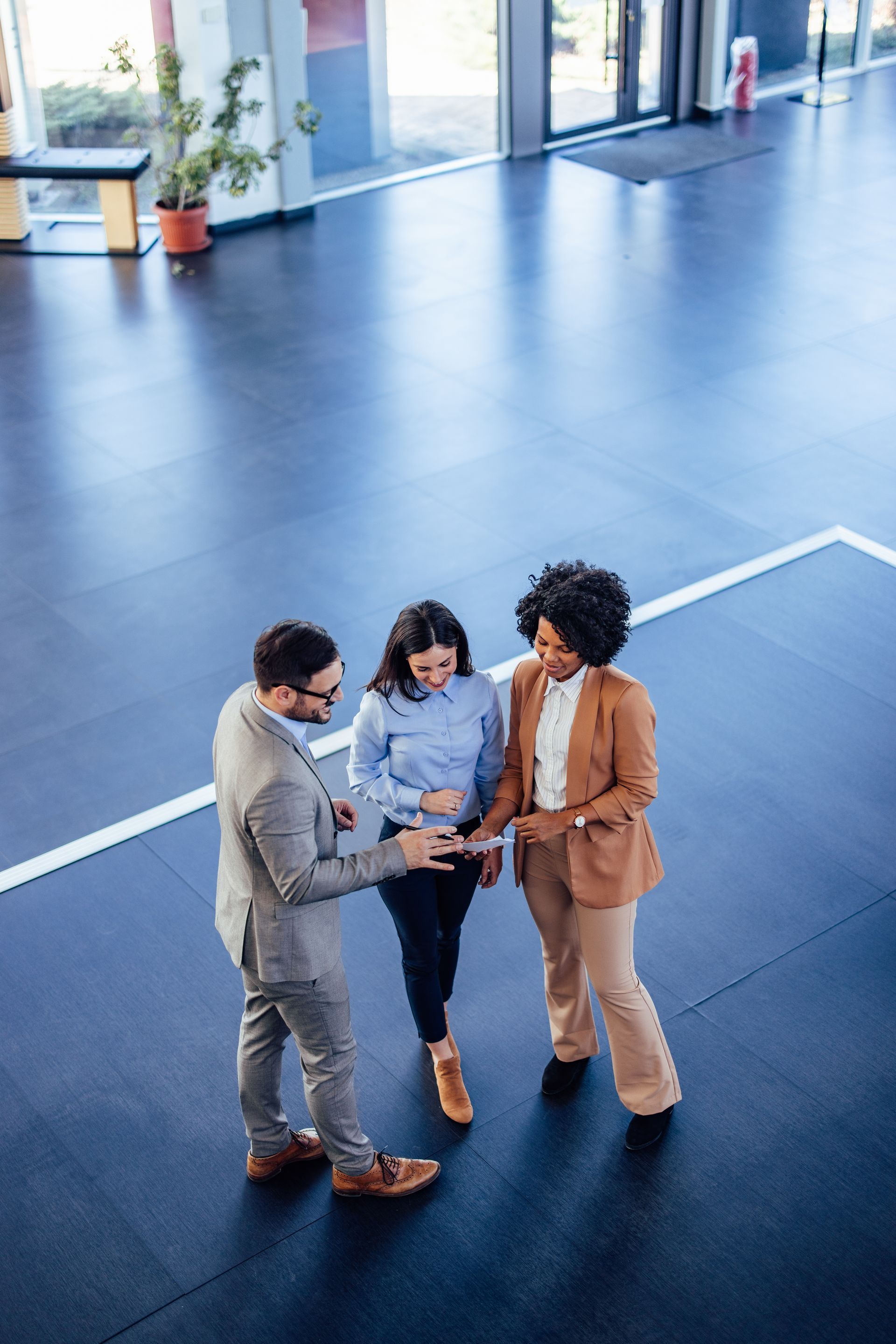 Three professionals in business attire stand in a circle on a large office floor, engaged in a discussion.