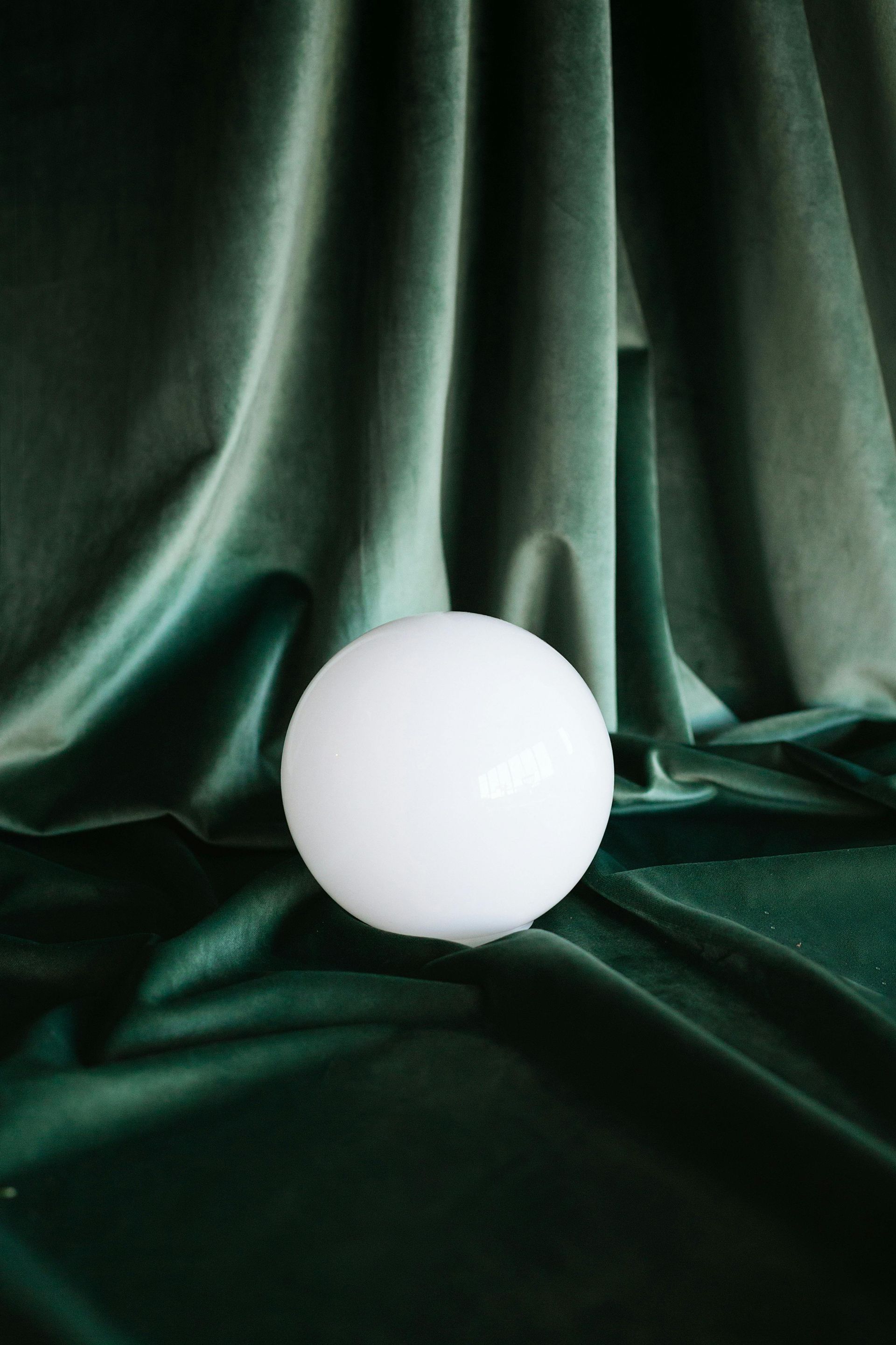 A white spherical object sits centered on draped, deep green velvet fabric.