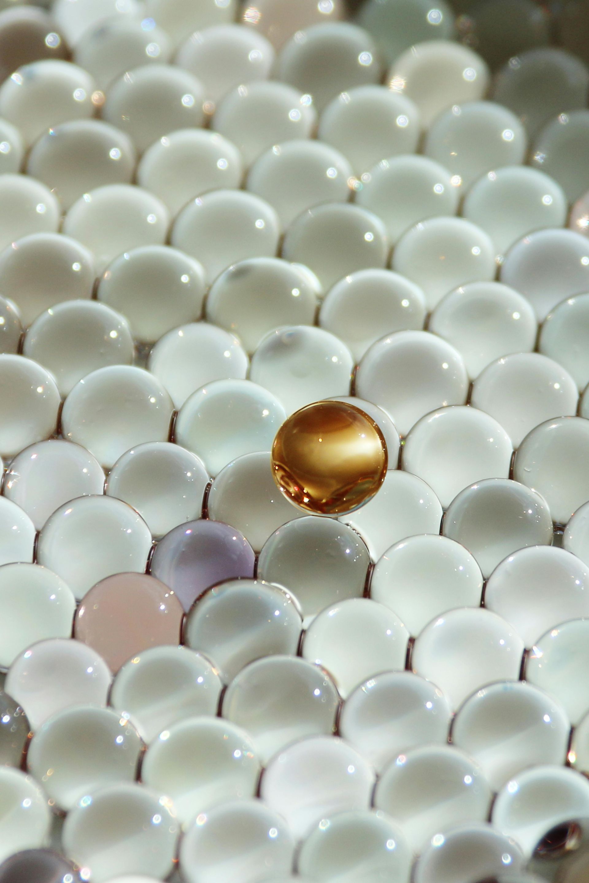 A single, translucent amber sphere sits atop a dense, repeating pattern of white and pale-pink translucent water beads.