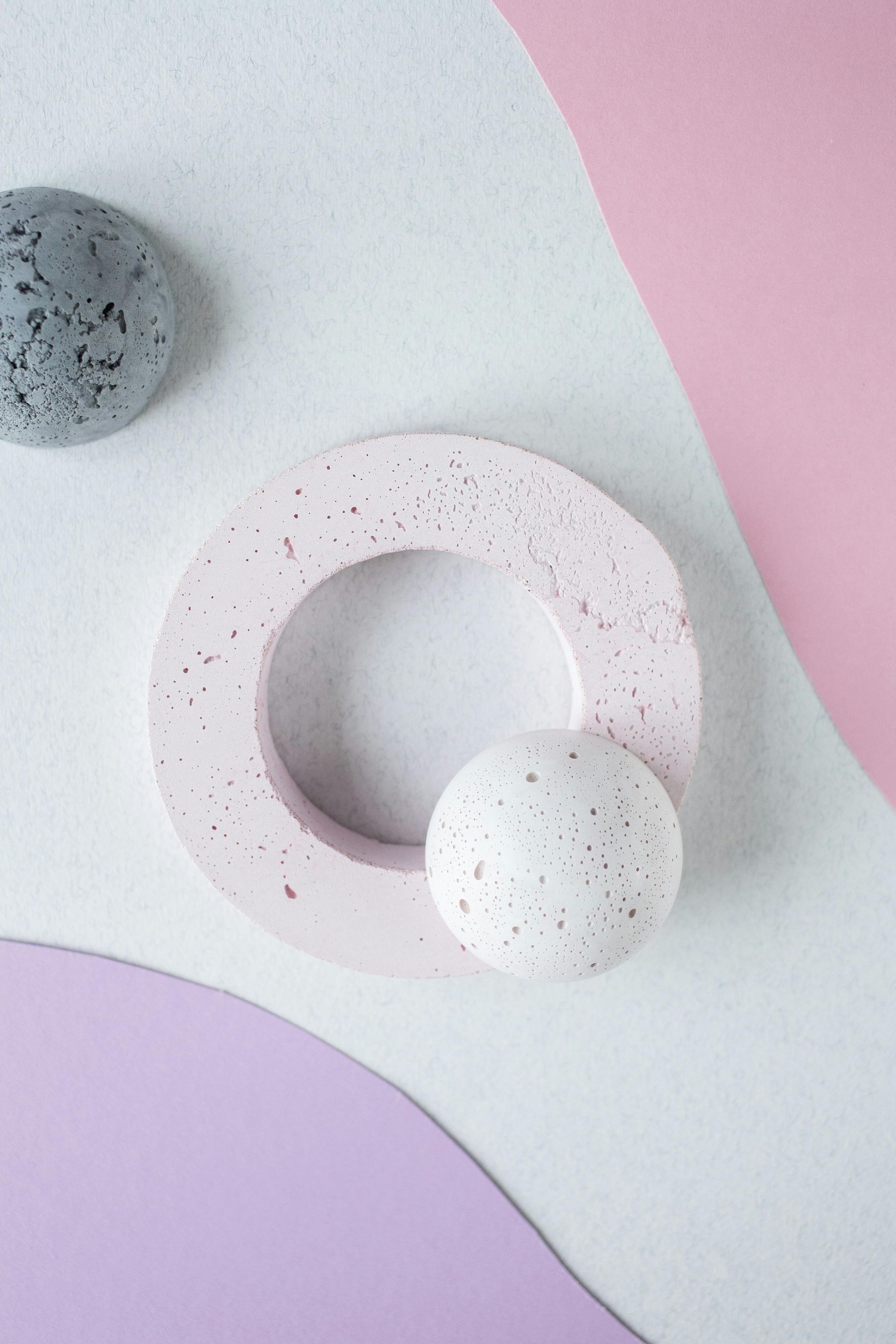 A flat-lay of speckled concrete decor, including a round frame and spheres in pastel pink, grey, and white.