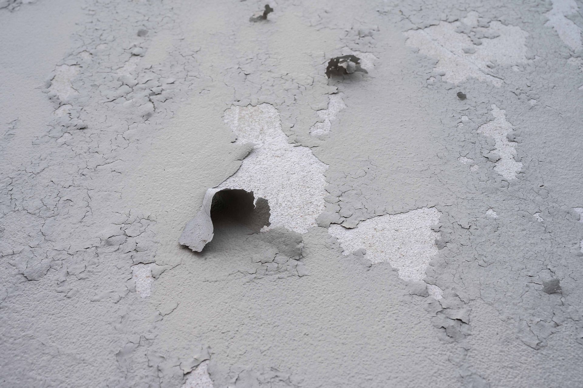 Mur en stuc gris et écaillé avec des trous révélant du plâtre blanc en dessous.