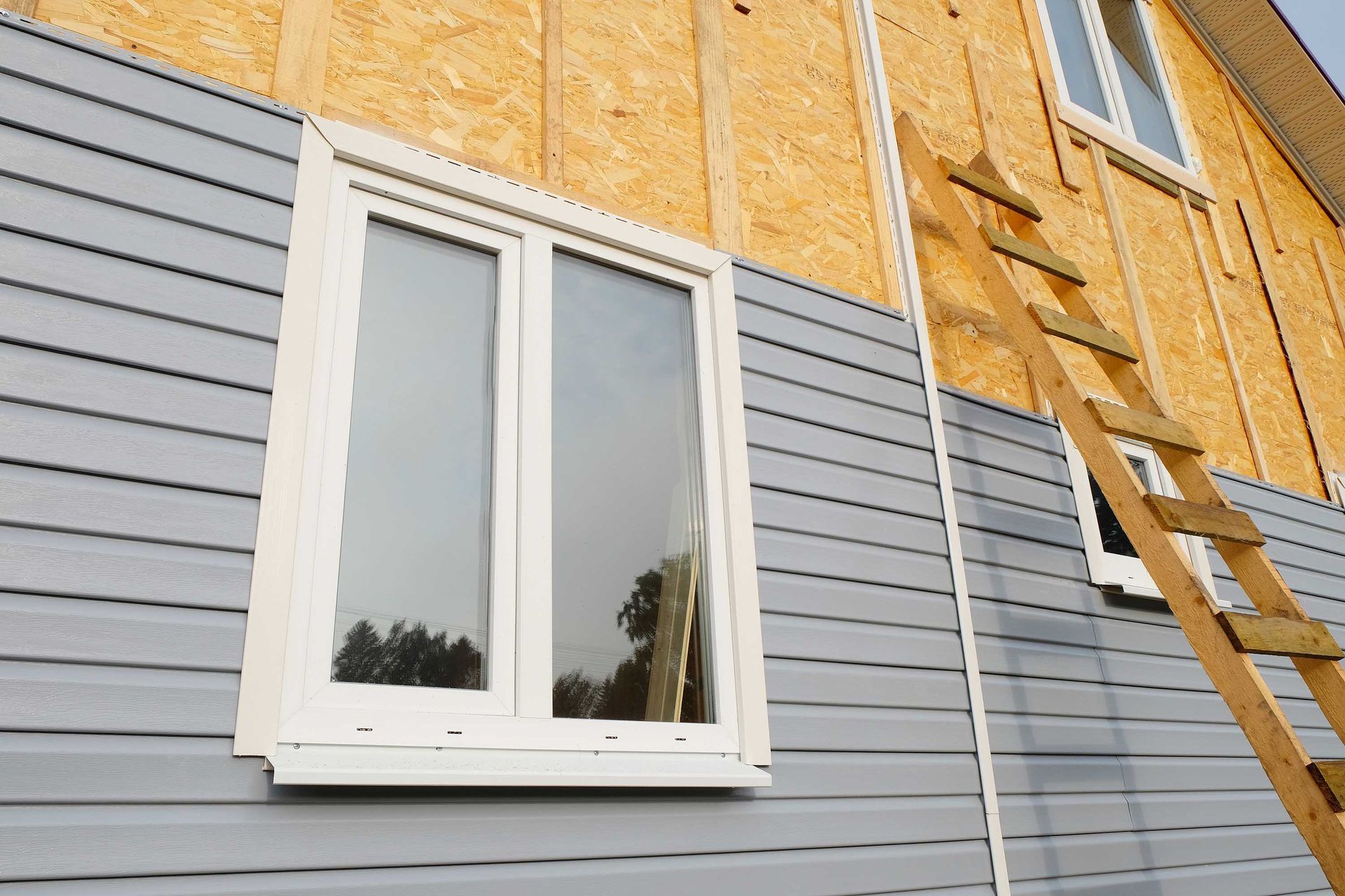 Une maison en construction avec un revêtement bleu, une fenêtre blanche et une échelle en bois.