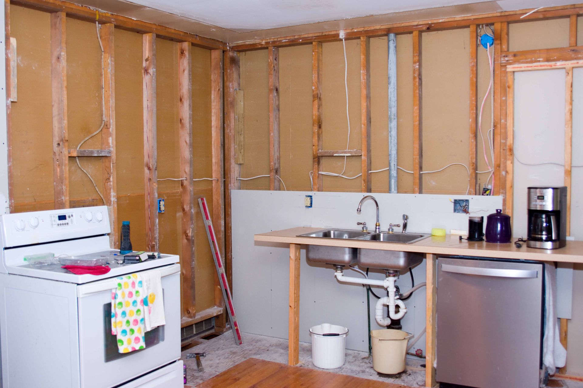 Cuisine vidée pour rénovation : charpentes apparentes, électroménager (four, évier, lave-vaisselle), plan de travail, câblage.
