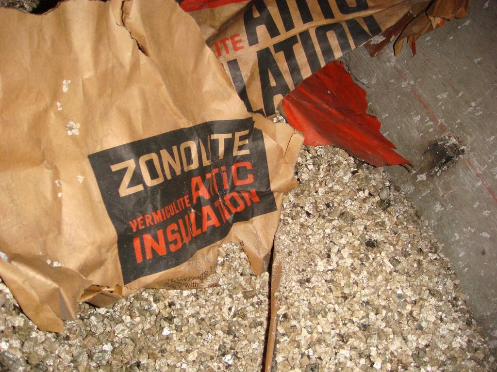 Sac étiqueté « Zonolite Vermiculite Attic Insulation » déchiré, révélant l'isolation.