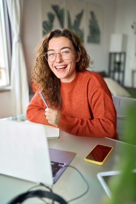 A woman is sitting at a desk with a laptop and a pen in her hand