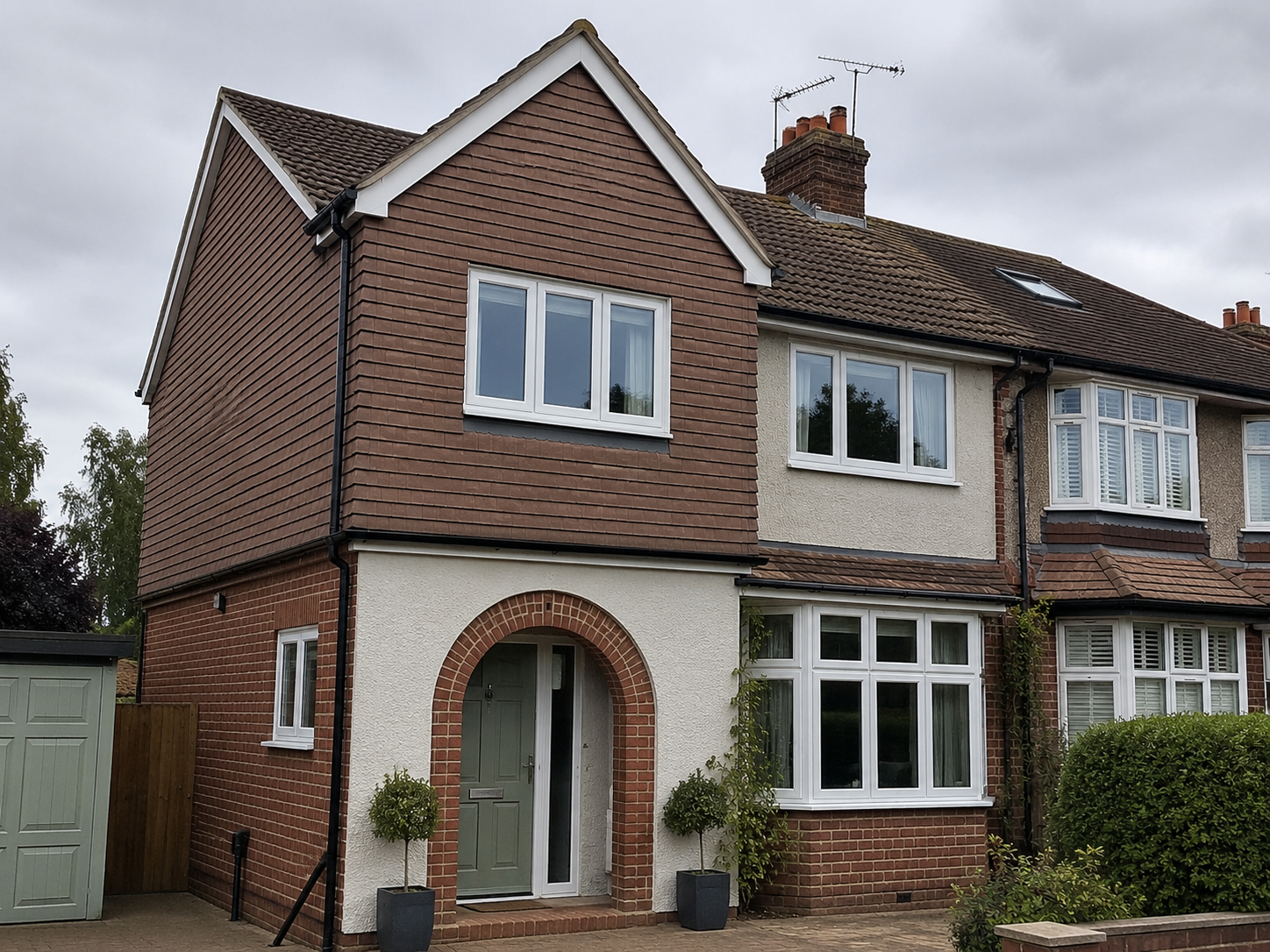 Semi-detached brick house with arched porch, white-framed windows, and a green side gate