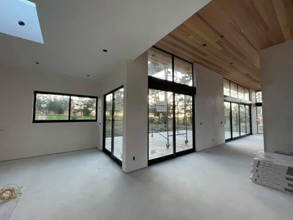 Unfinished interior space with white walls, large black-framed windows, and a sloped wood-paneled ceiling.