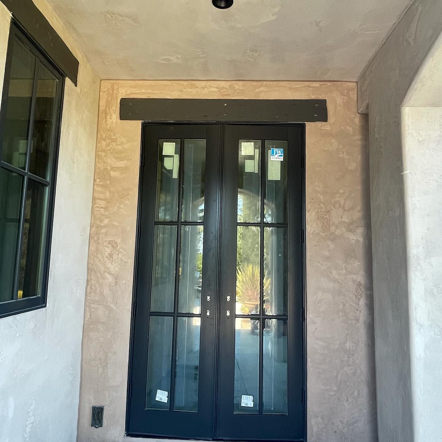 Double black-framed glass entry doors with a rectangular transom window on a textured, light-colored stucco porch.
