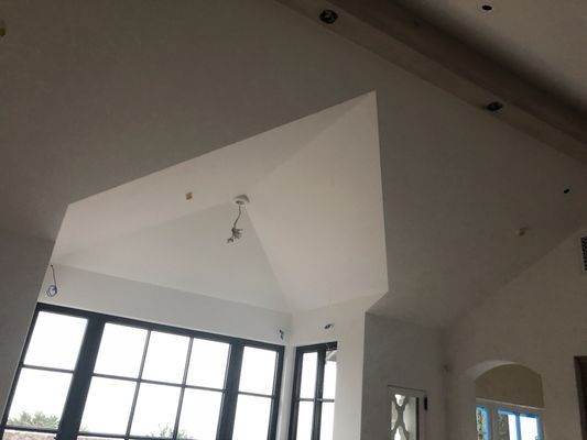 Interior view of a room with a high, vaulted ceiling and large black-framed windows under construction.