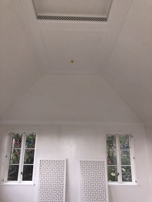 A white room with a vaulted ceiling, a skylight, two windows, and two decorative white lattice panels leaning against walls.