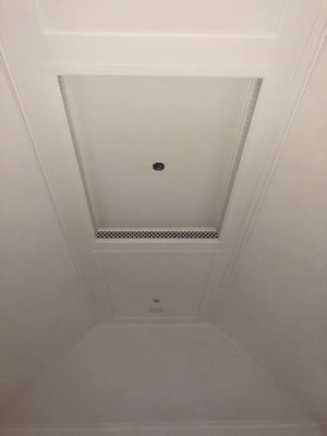 A low-angle view of a white, recessed tray ceiling featuring a central light fixture and a linear ventilation vent.