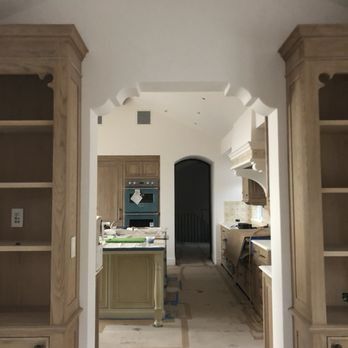 A view through a decorative arched doorway into a kitchen featuring wooden cabinets, an island, and a dark arched door.