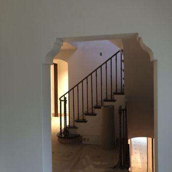 A staircase with a dark metal railing seen through a decorative, white-trimmed arched doorway.