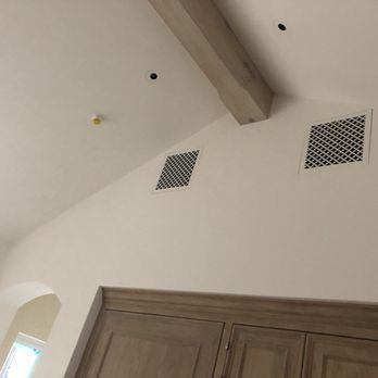 Interior view of a slanted white ceiling with a wooden beam, two square air vents, recessed lights, and a smoke detector.