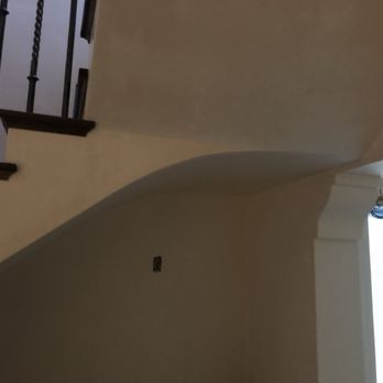 An indoor view of a staircase with dark metal railings, a curved drywall arch, and a white pillar in a beige room.