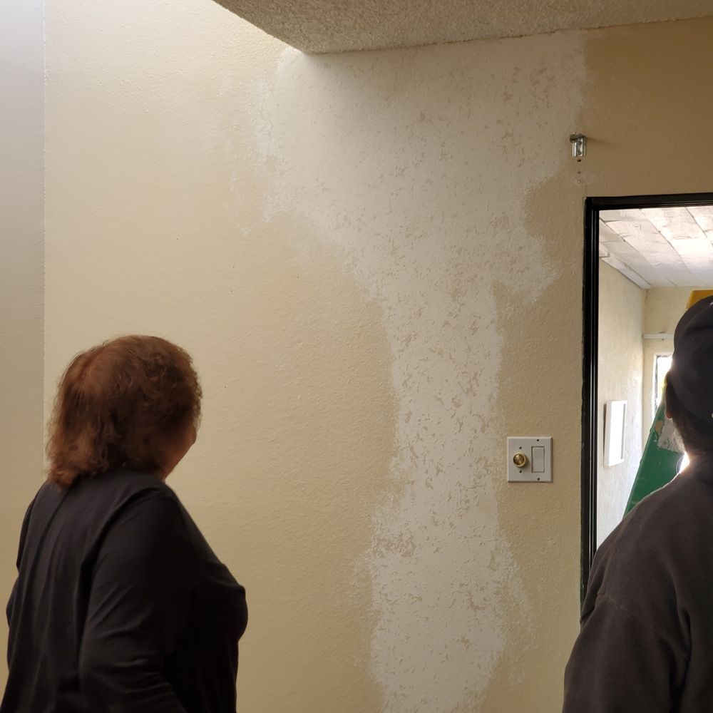 A man and a woman are standing in a hallway looking at a wall