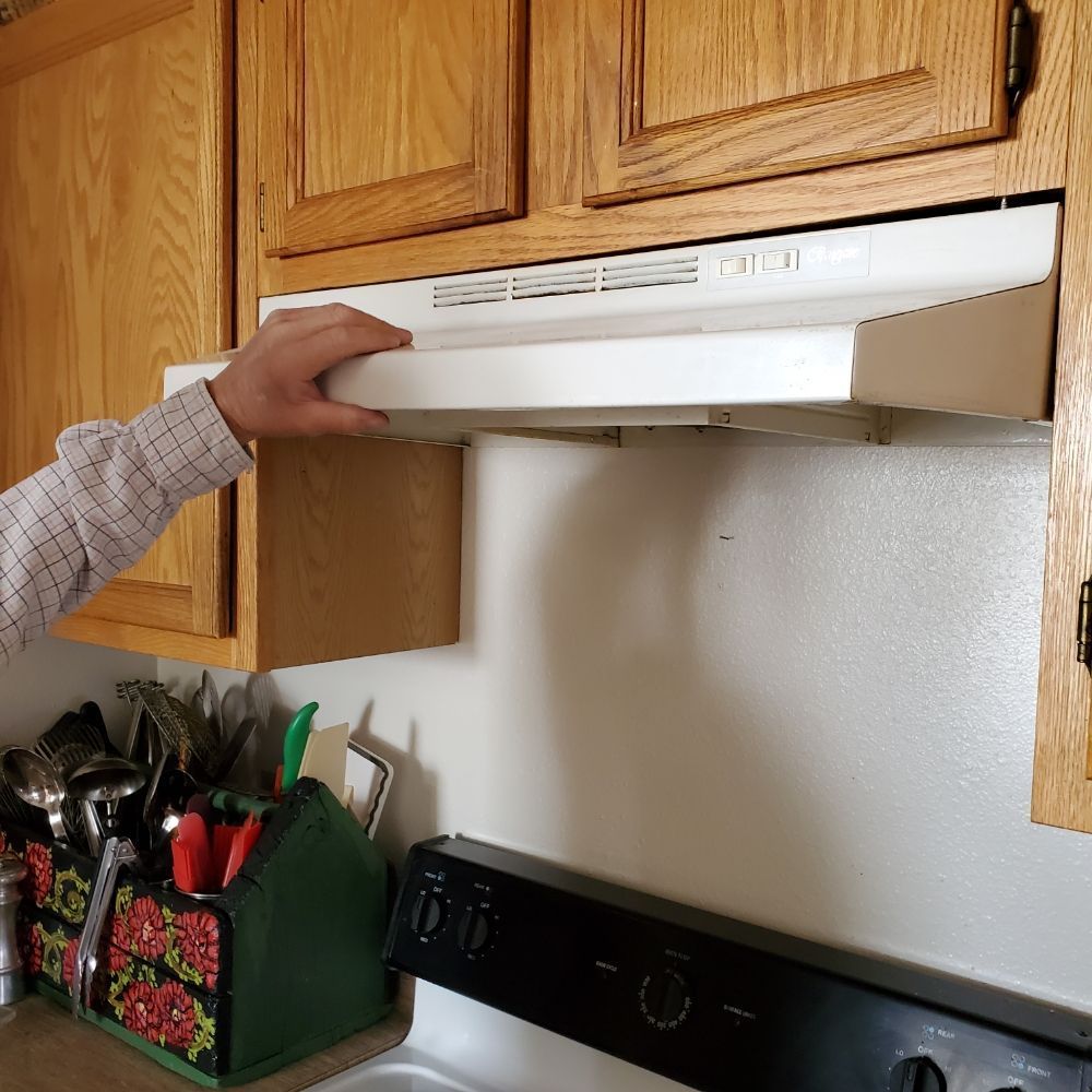 A person is opening a stove hood in a kitchen