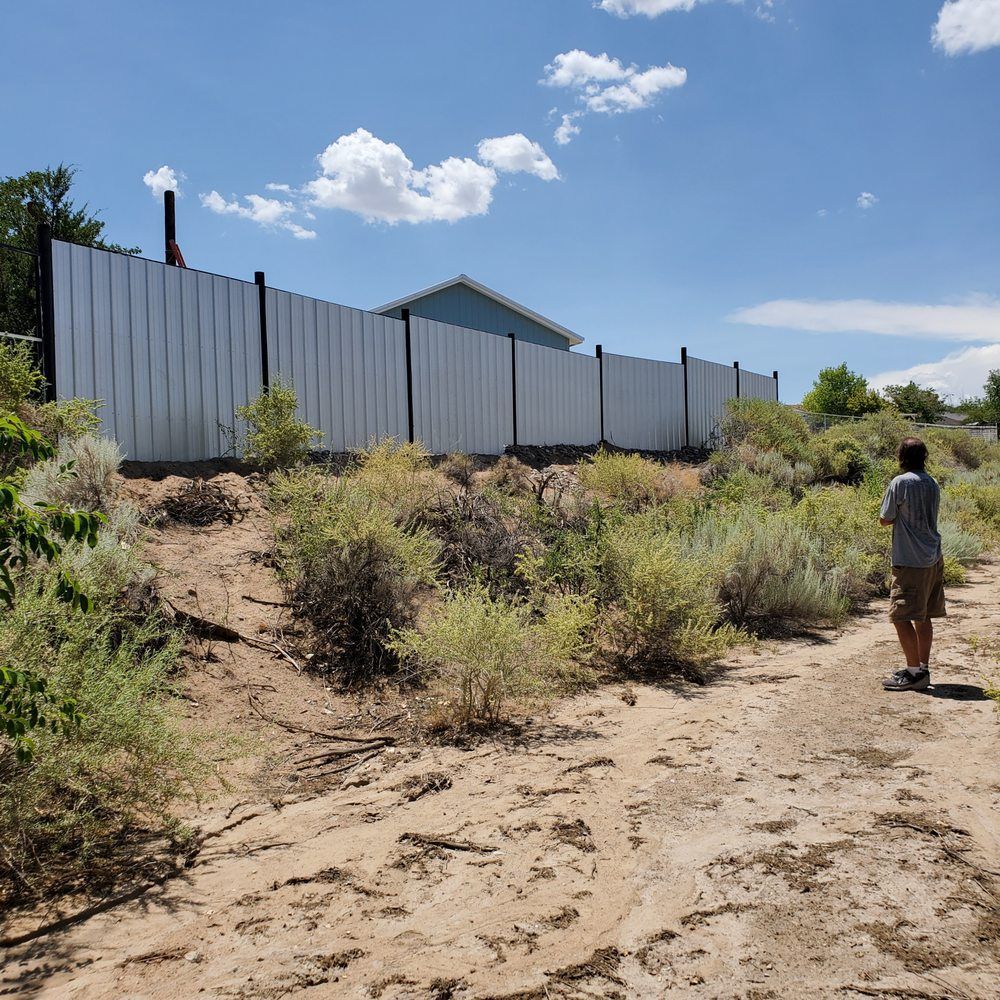 A man is standing on a dirt path in front of a fence.