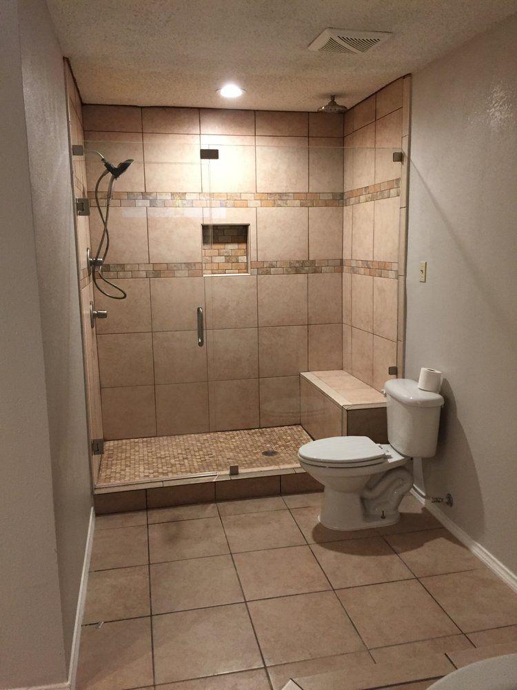 A bathroom with a toilet , shower and bench.