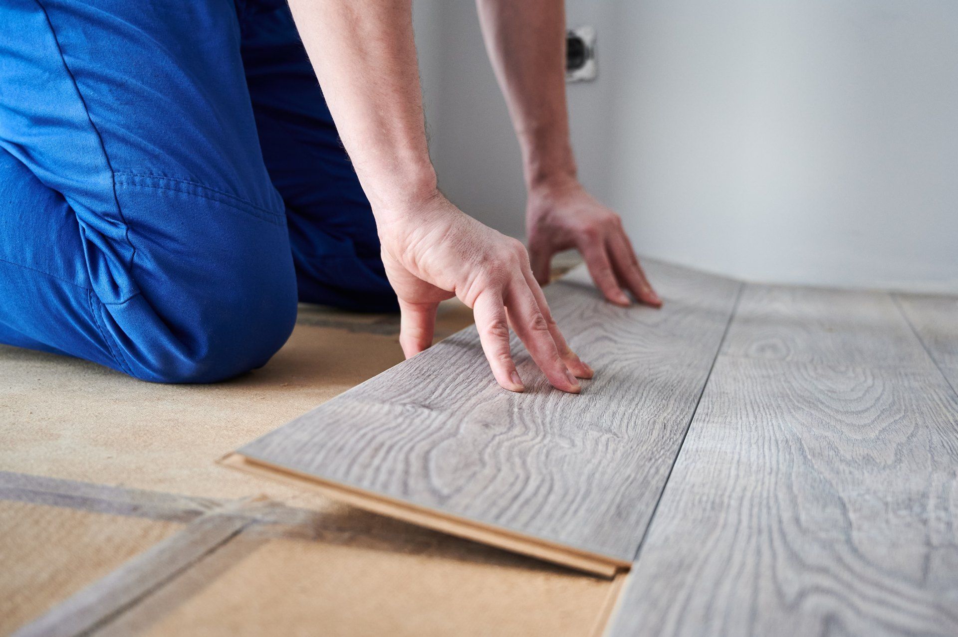 A person is kneeling down to install a wooden floor.