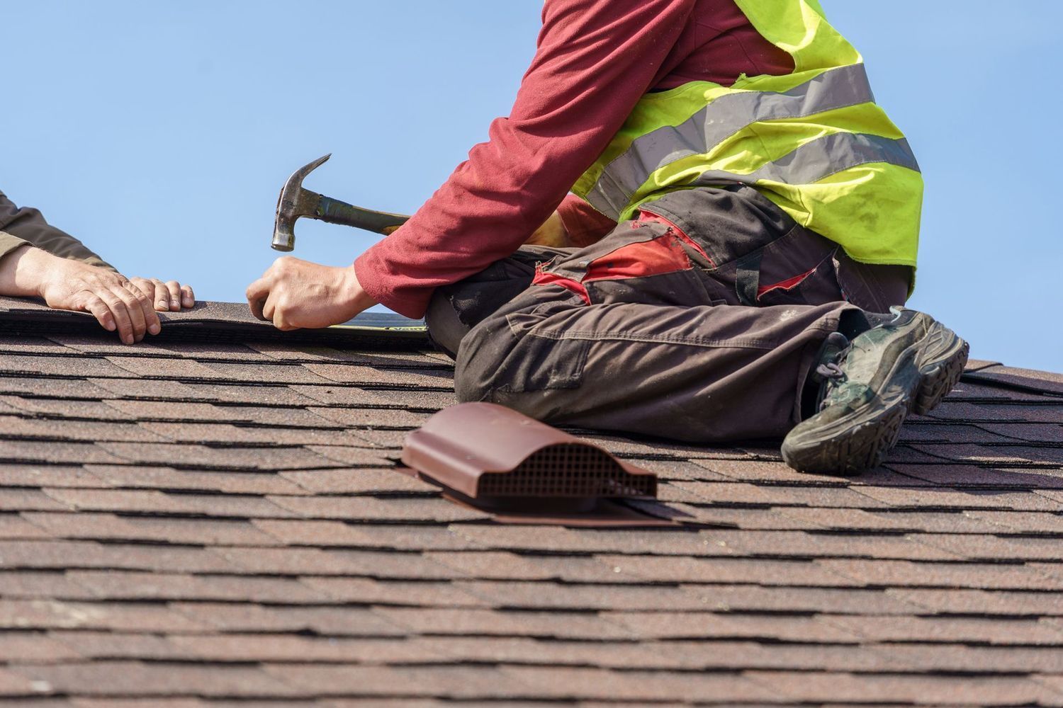 A man is kneeling on a roof with a hammer.