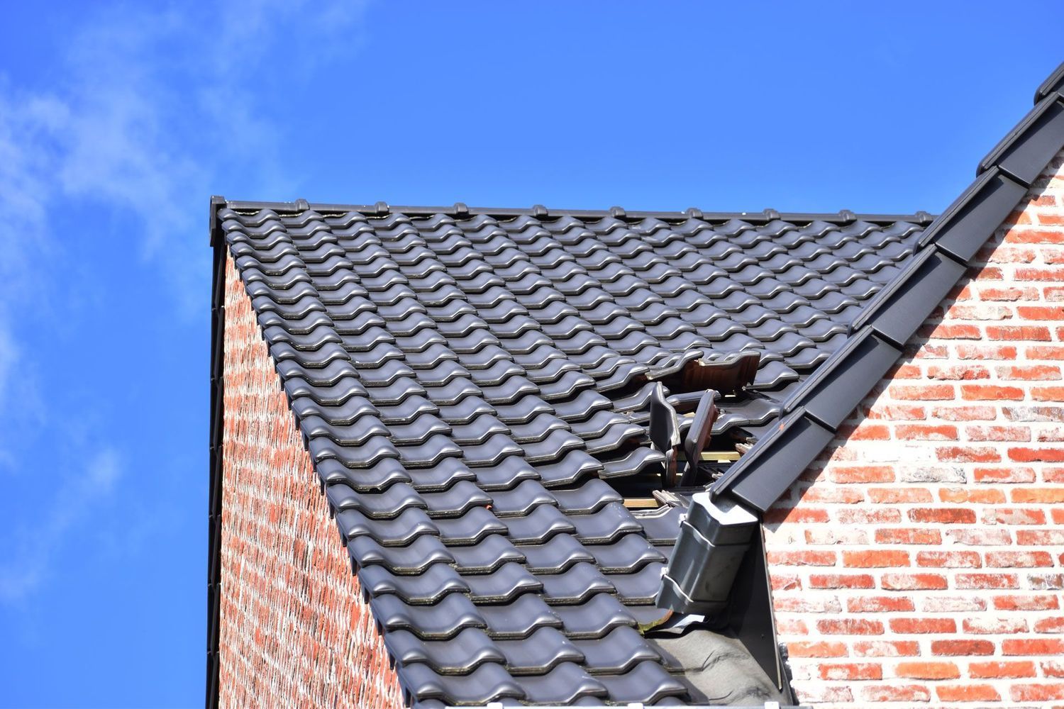 A brick building with a black tiled roof and a blue sky in the background.