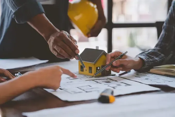 A group of people are sitting at a table looking at a model house.