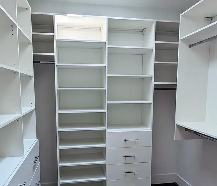 White built-in closet with shelves, drawers, and hanging rods. Well-lit, organized storage space.