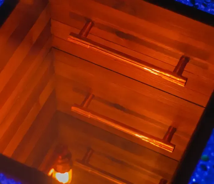 Wooden box interior with two horizontal copper handles, lit by a warm light at the bottom.