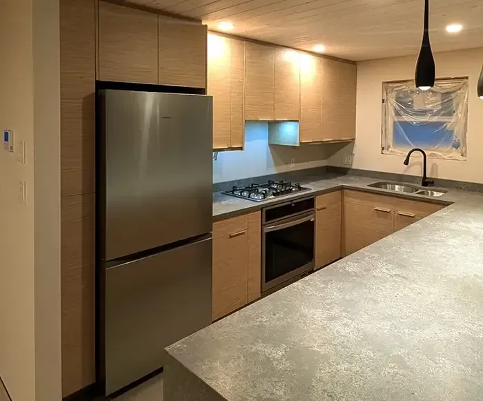 Modern kitchen with light wood cabinets, stainless steel appliances, and gray countertops.