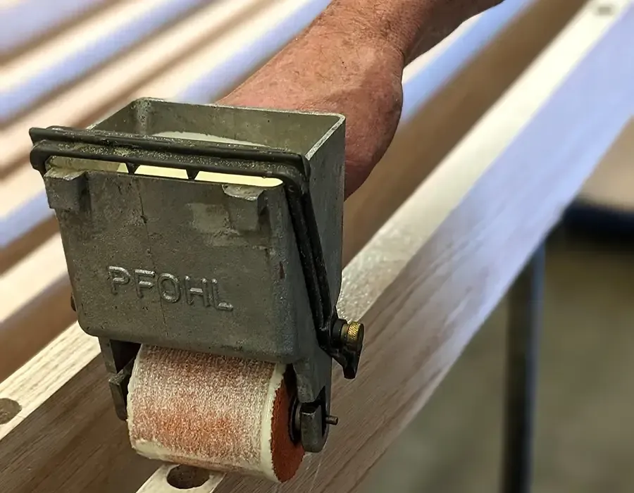 Person using a Pfohl roller to apply a clear finish to wooden boards in a workshop.
